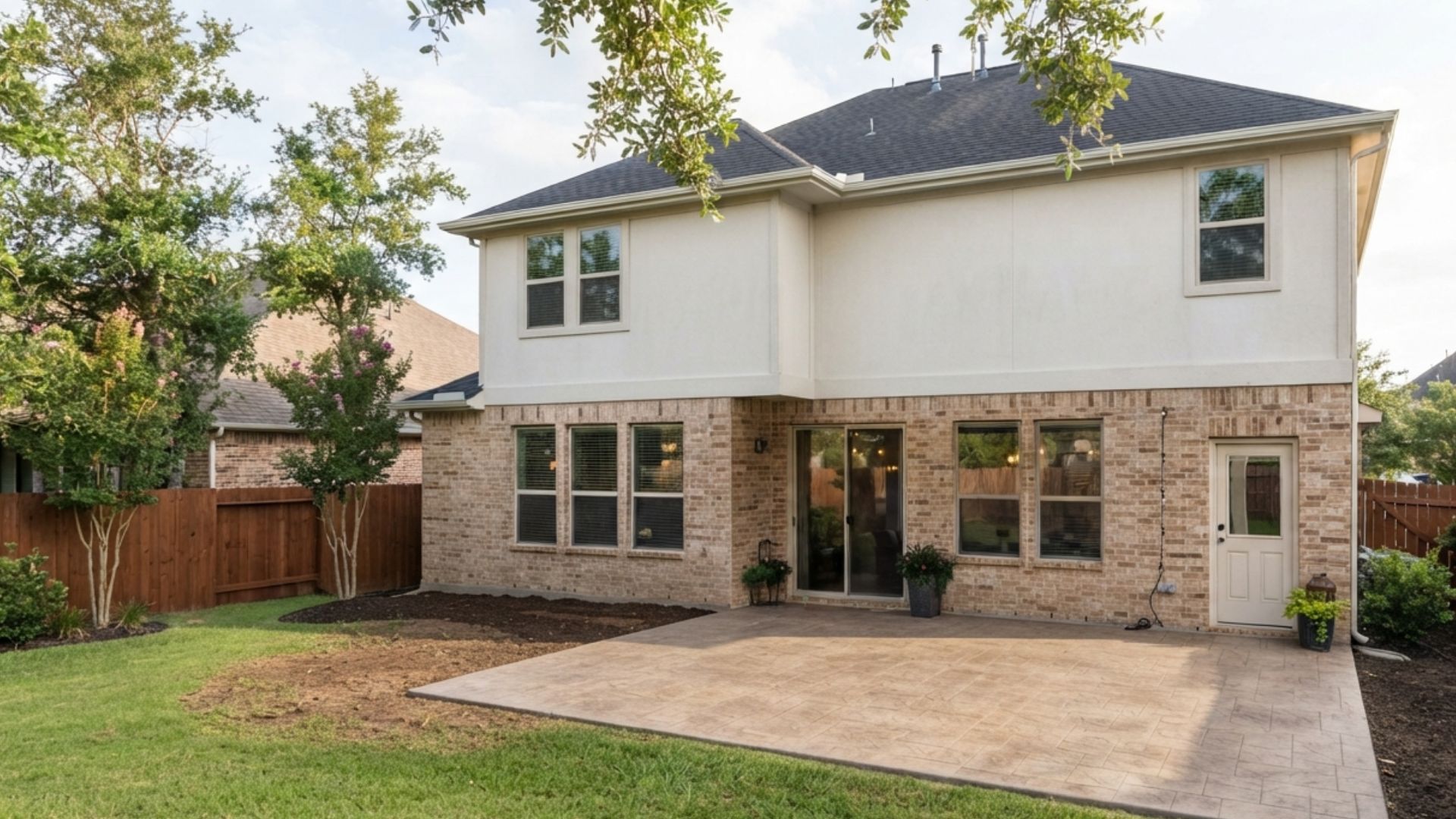 Rear view of a suburban brick and stucco home in Katy, Texas, showing an empty stamped concrete patio without a cover, furniture, or plants.