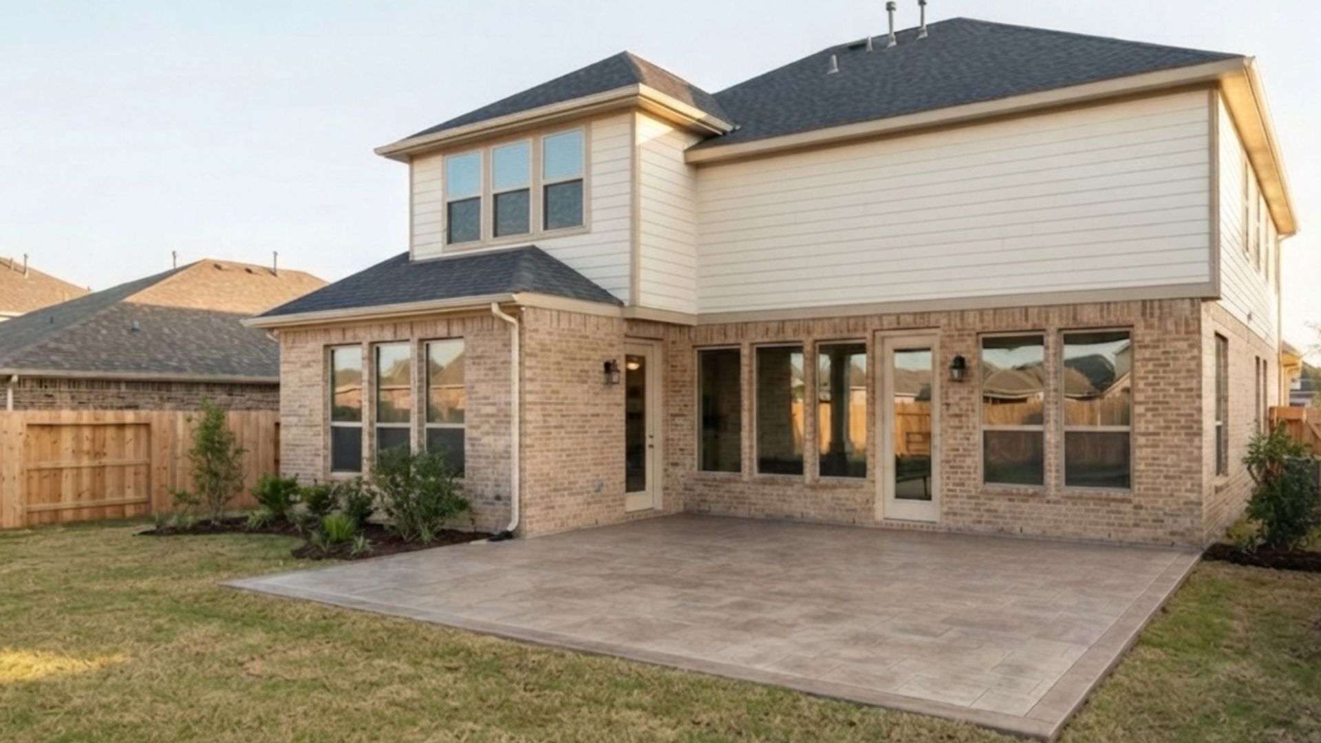Rear view of a two-story suburban home with an open concrete patio before custom patio cover installation in Avalon at Cypress