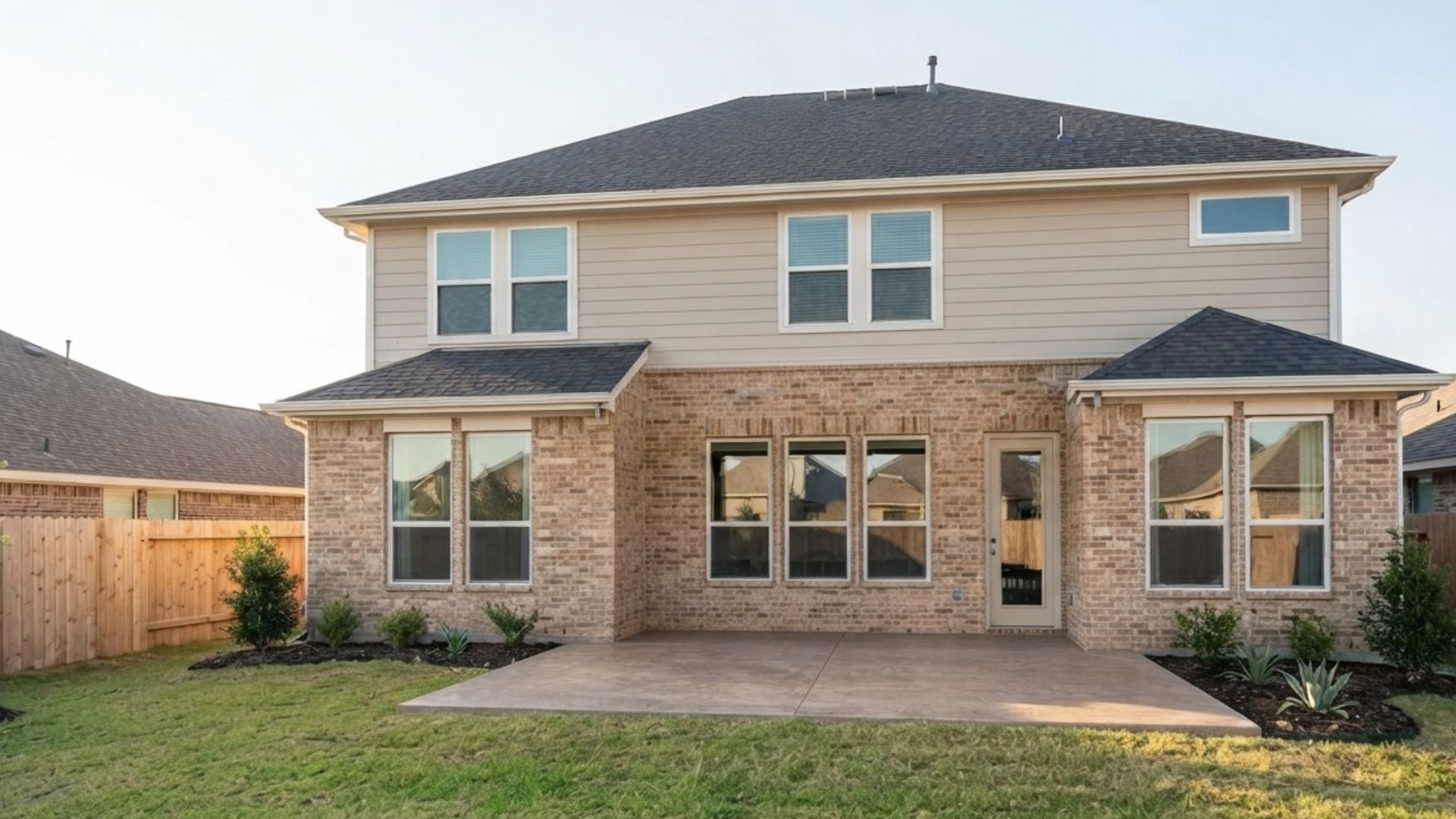 Backyard of a two-story residential home with a concrete patio slab, lawn, and wood fence in Dunham Pointe, Cypress, Texas, showing the backyard before adding a custom patio cover or outdoor kitchen.